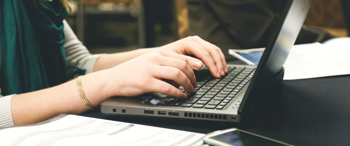 Vrouw maakt lesvoorbereiding met computer en een notitieblok erbij. Ze is aan het typen.