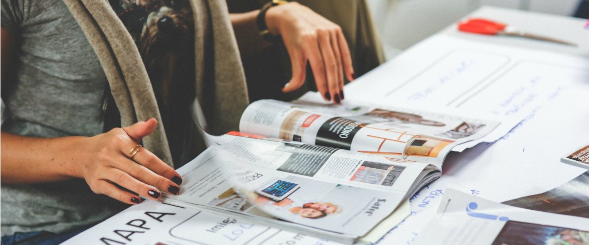 Vrouw werkt in een tijdschrift, je ziet ook een schaar en notities, ze maakt een lesvoorbereiding.