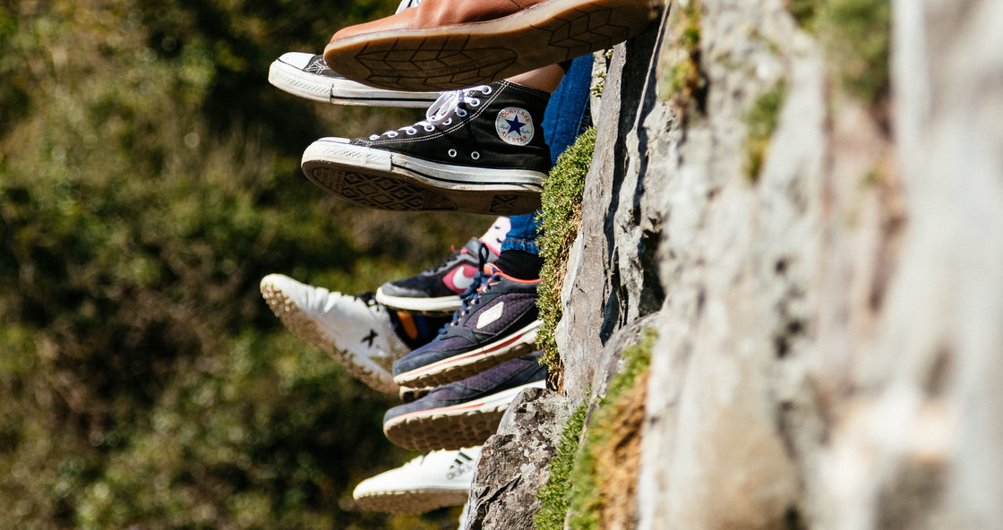 Schoenen van jongeren die op een stenen afsluiting zitten.