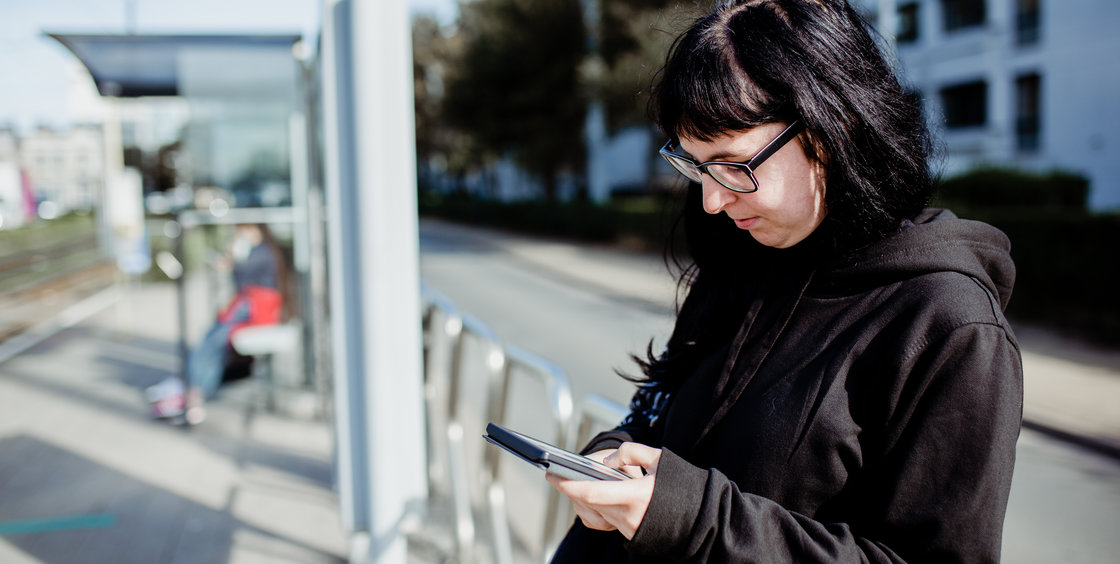 Vrouw leest een e-boek aan de tramhalte.