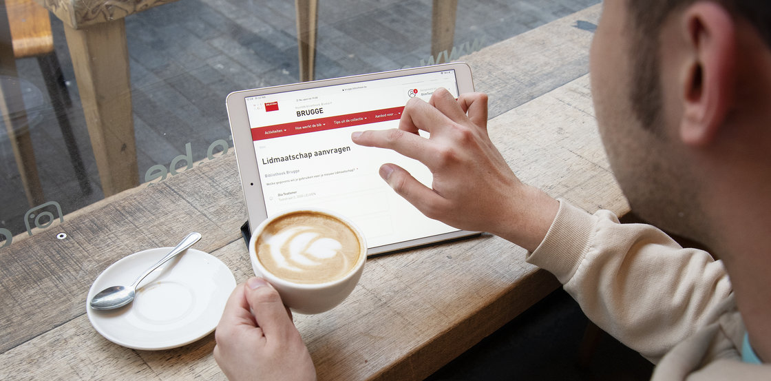 Man heeft koffie in de hand en schrijft online in via Mijn Bibliotheek.