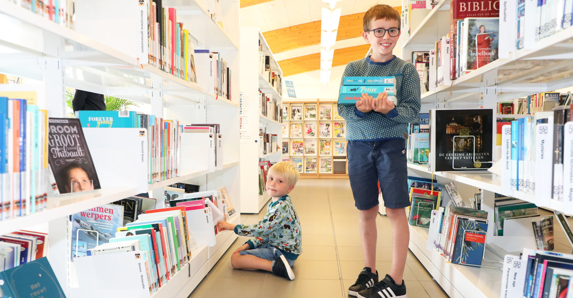 Kindjes in de bib tussen de rekken met boeken en met boeken in hun handen.