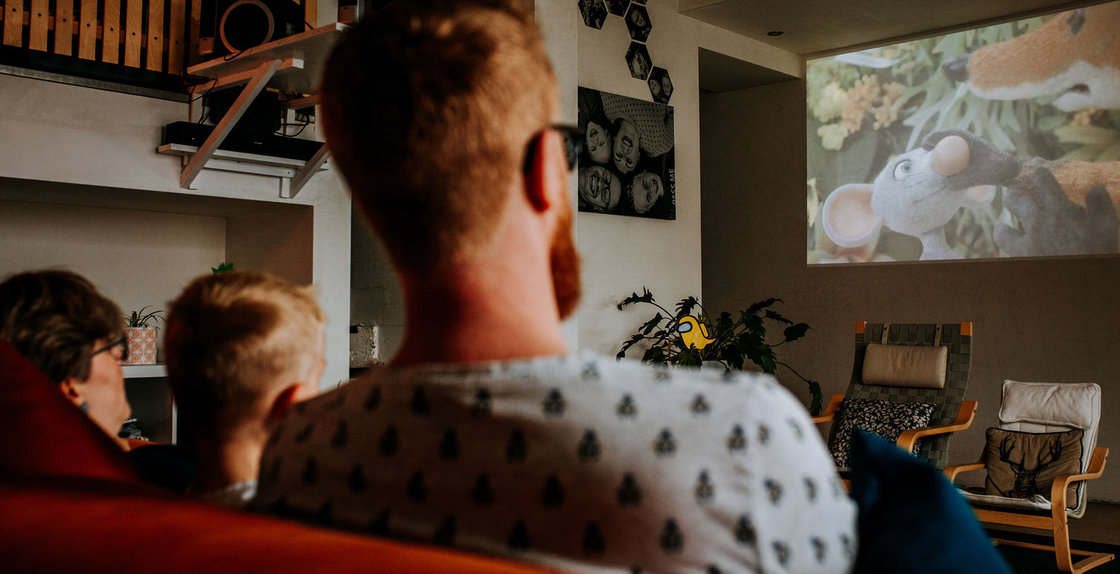 Gezin kijkt naar een familiefilm op groot scherm in de woonkamer.