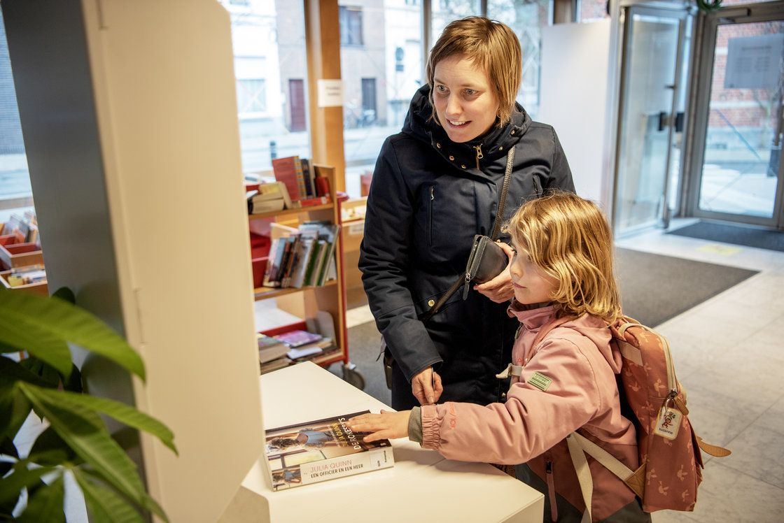 Moeder en dochter scannen een boek in aan de zelfscanautomaat in de bibliotheek