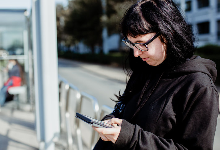 Vrouw leest een e-boek aan de tramhalte.