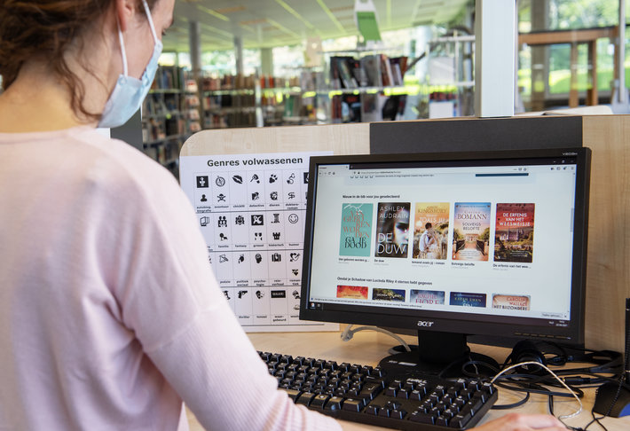Vrouw bekijkt leestips van Mijn Leestipper op dekstop in de bib, achteraanzicht.