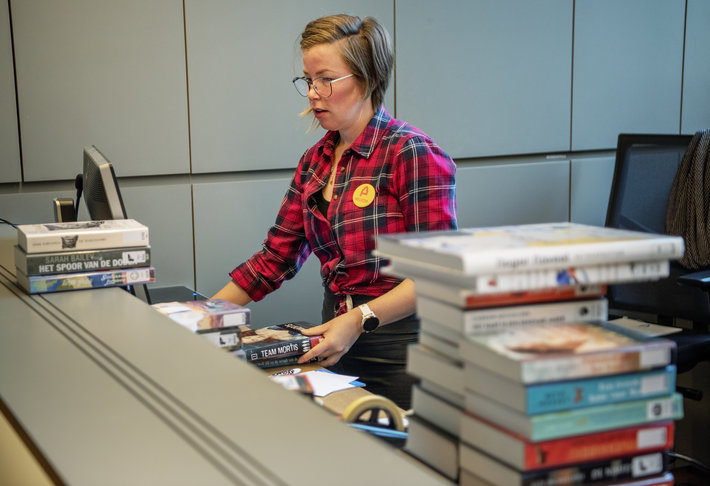 medewerker werkt met stapels boeken aan de balie van de bib