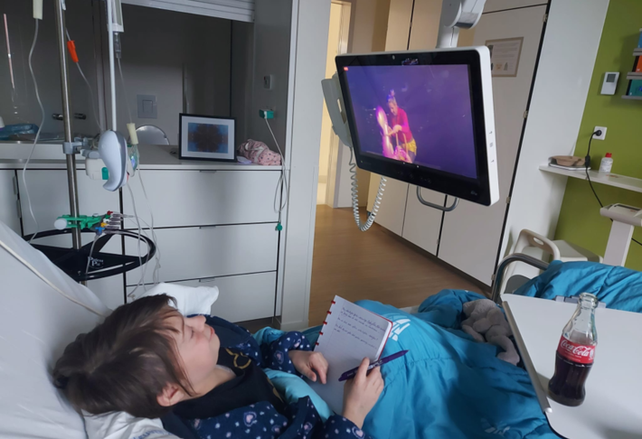 Meisje kijkt vanuit haar ziekenbed op een tv-scherm naar de livestream van de voorstelling Kameleonie