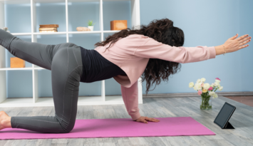 Vrouw doet yoga met een tablet voor haar matje.