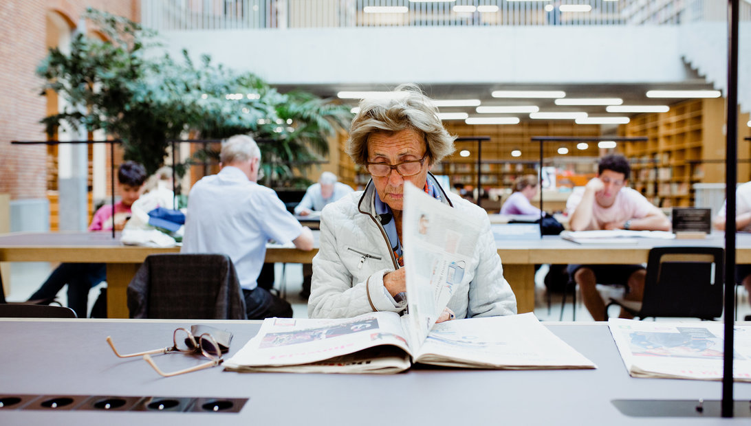 Vrouw die leest in een krant in de bib